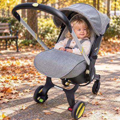 Couvre jambe poussette gris installé sur la partie basse de l’assise avec bébé dans un parc en automne