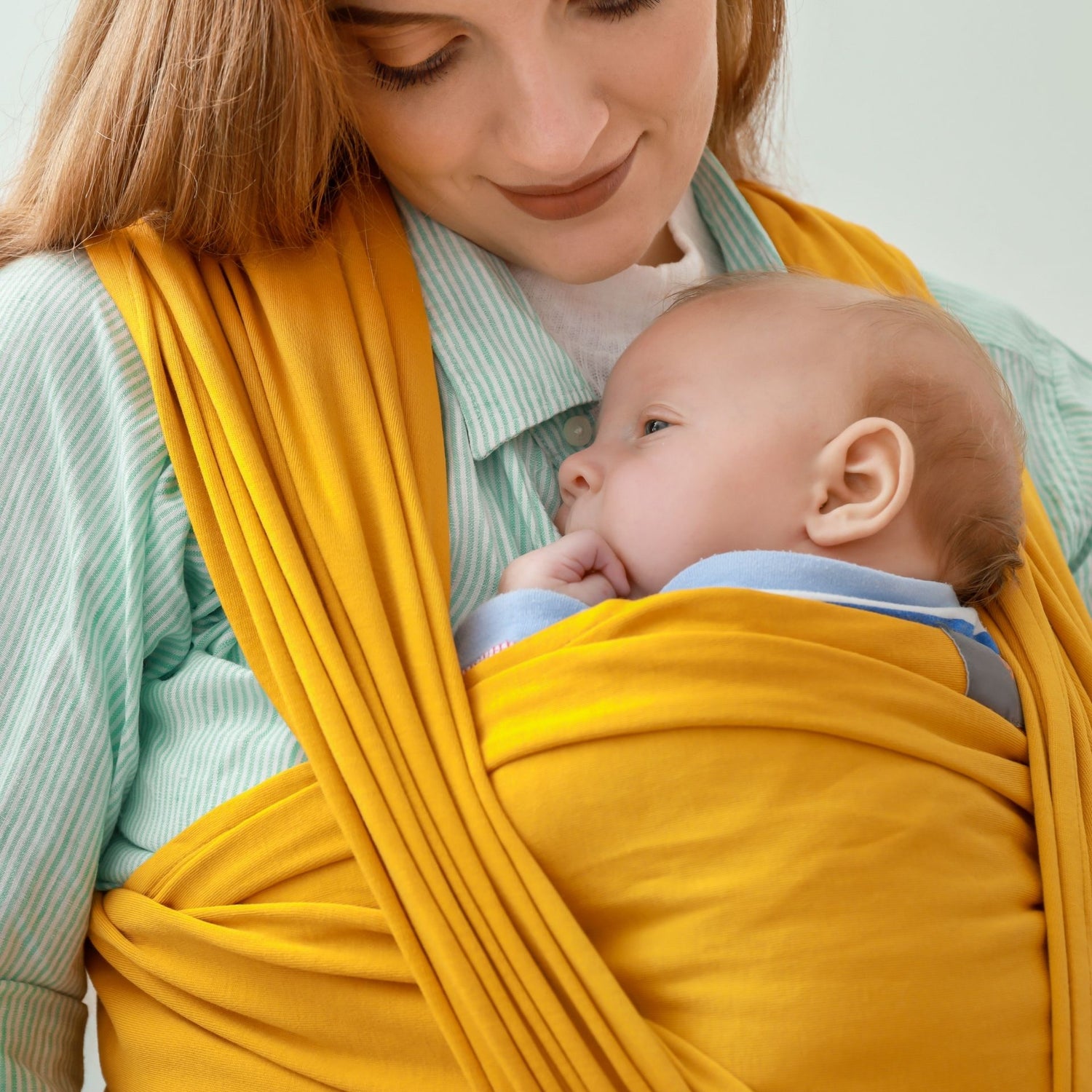 Maman portant un nourrisson contre elle dans une écharpe de portage jaune moutarde, moment de tendresse et proximité

