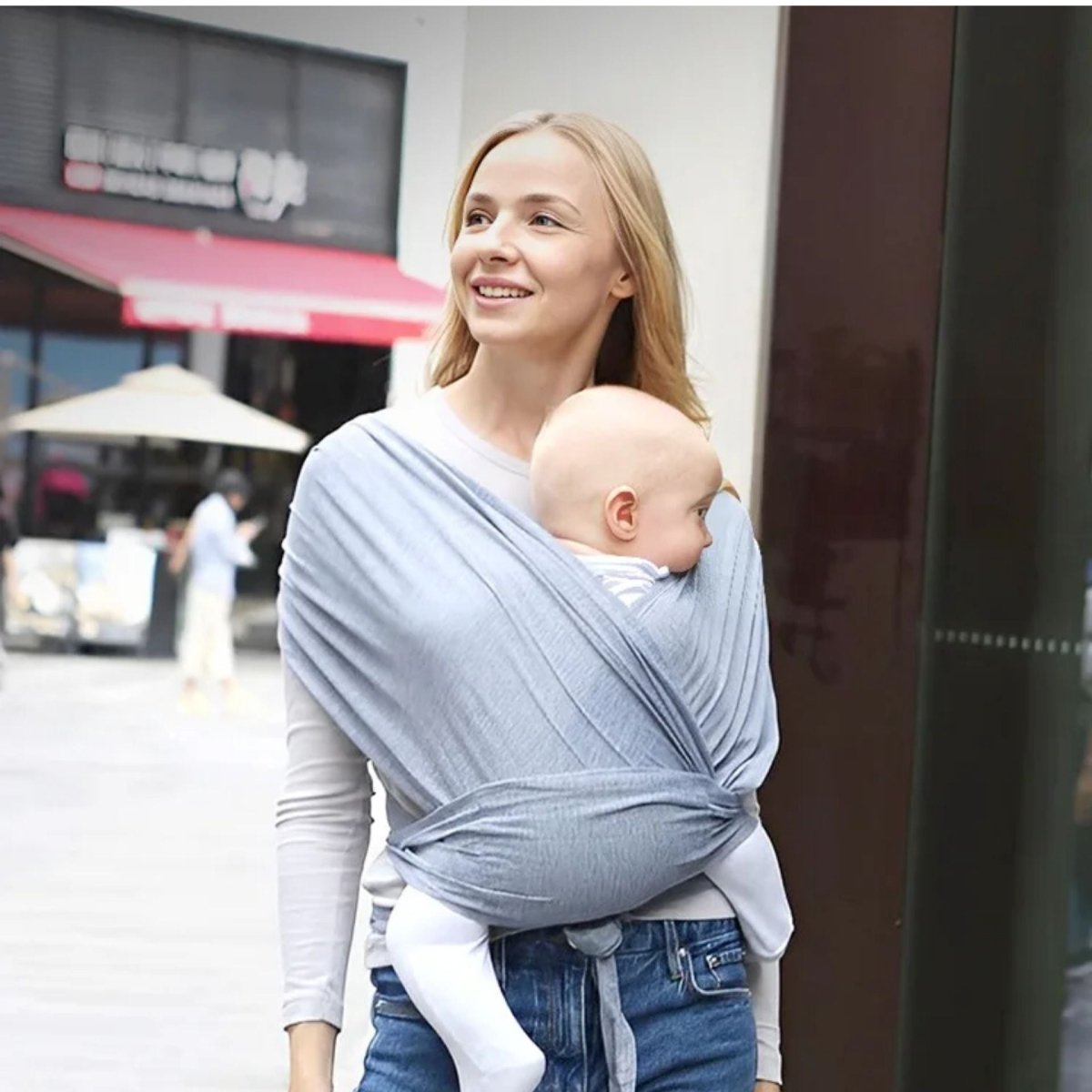 Maman en balade urbaine portant une echarpe de portage gris clair avec bebe