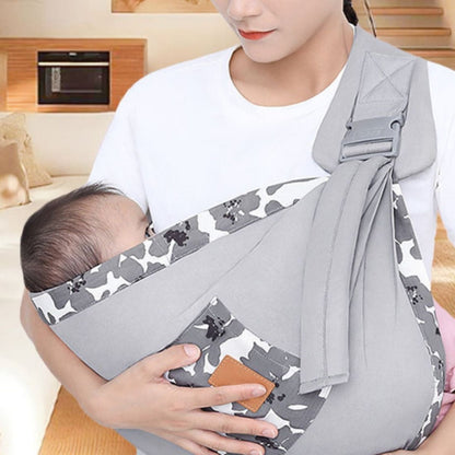 echarpe de portage gris camouflage en intérieur, bébé calé dans la poche côté droit, tissu gris clair avec bord blanc imprimé