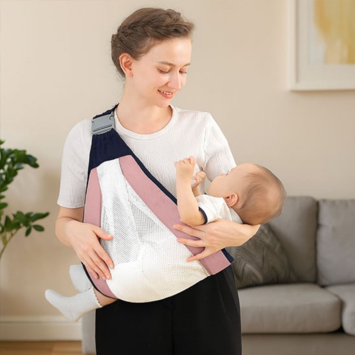 Maman souriante avec son bébé allongé dans une echarpe rose et blanche à l’intérieur