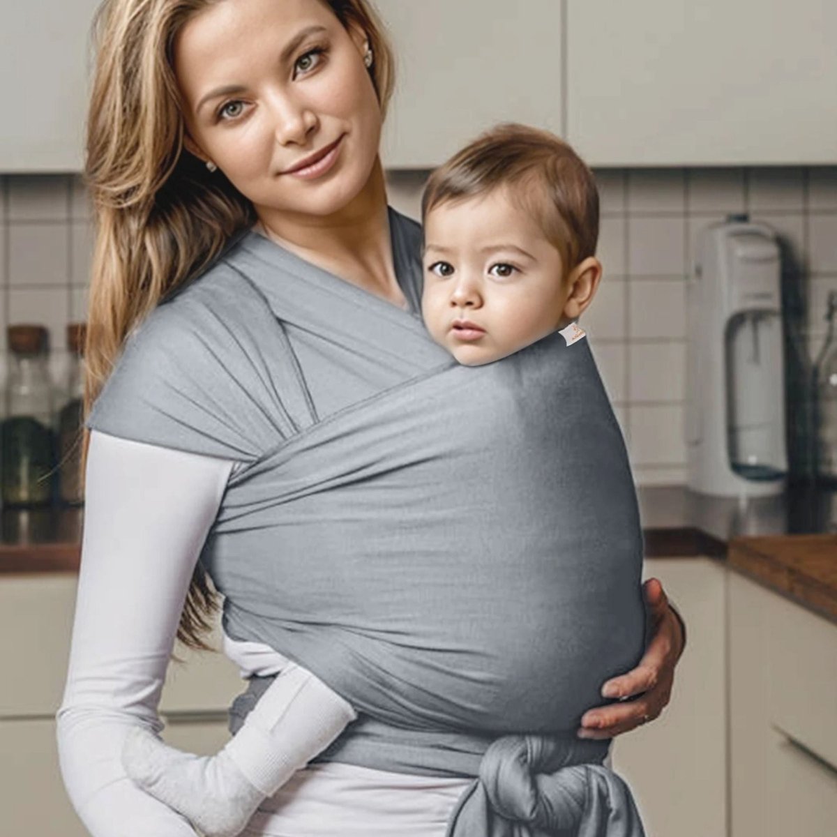 Maman en cuisine avec bébé contre elle dans une echarpe de portage gris clair croisée