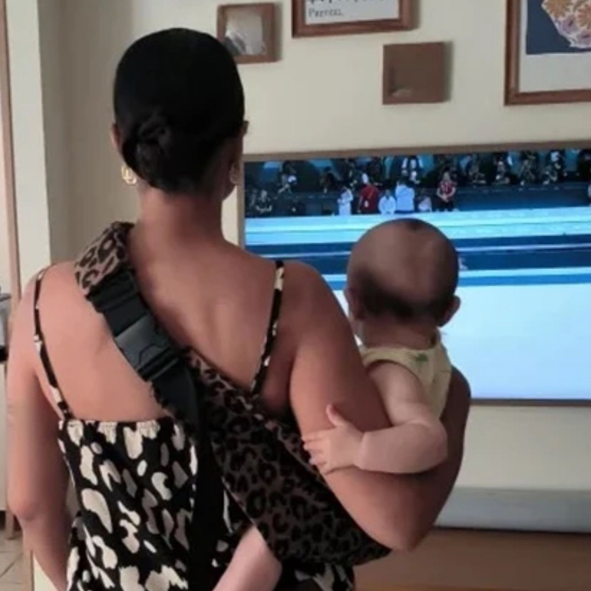 Écharpe de portage léopard portée en intérieur par une maman de dos tenant son bébé