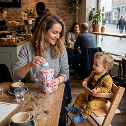 Étui imprimé pour biberon rose utilisé avec un biberon lors d’une sortie au café