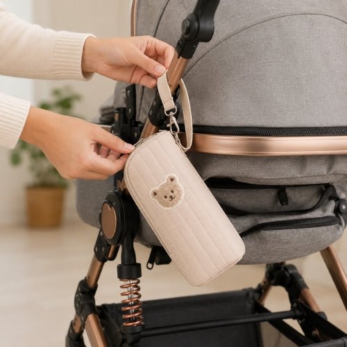 Étui matelassé pour biberon beige avec écusson ourson attaché à une poussette par sa sangle