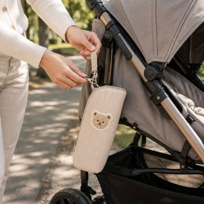 Étui matelassé pour biberon beige avec sangle et attache métallique près d’une poussette