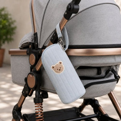 Étui matelassé pour biberon bleu avec écusson ourson fixé à une poussette par sa sangle