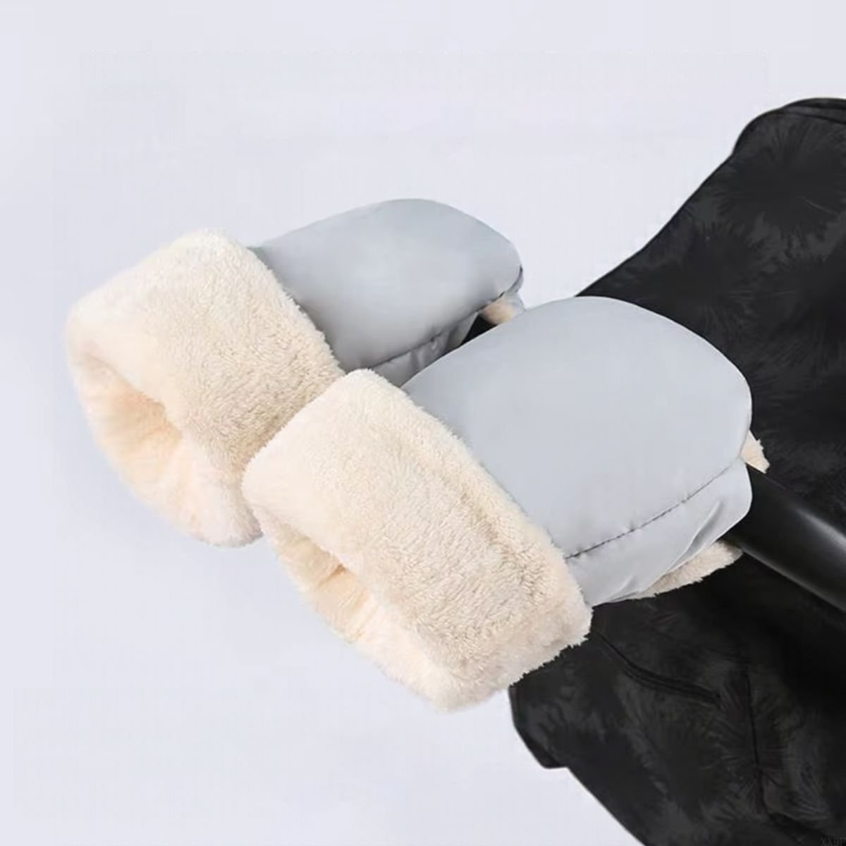 Paire de moufles de poussette gris clair avec ouvertures blanches duveteuses, installées sur le guidon