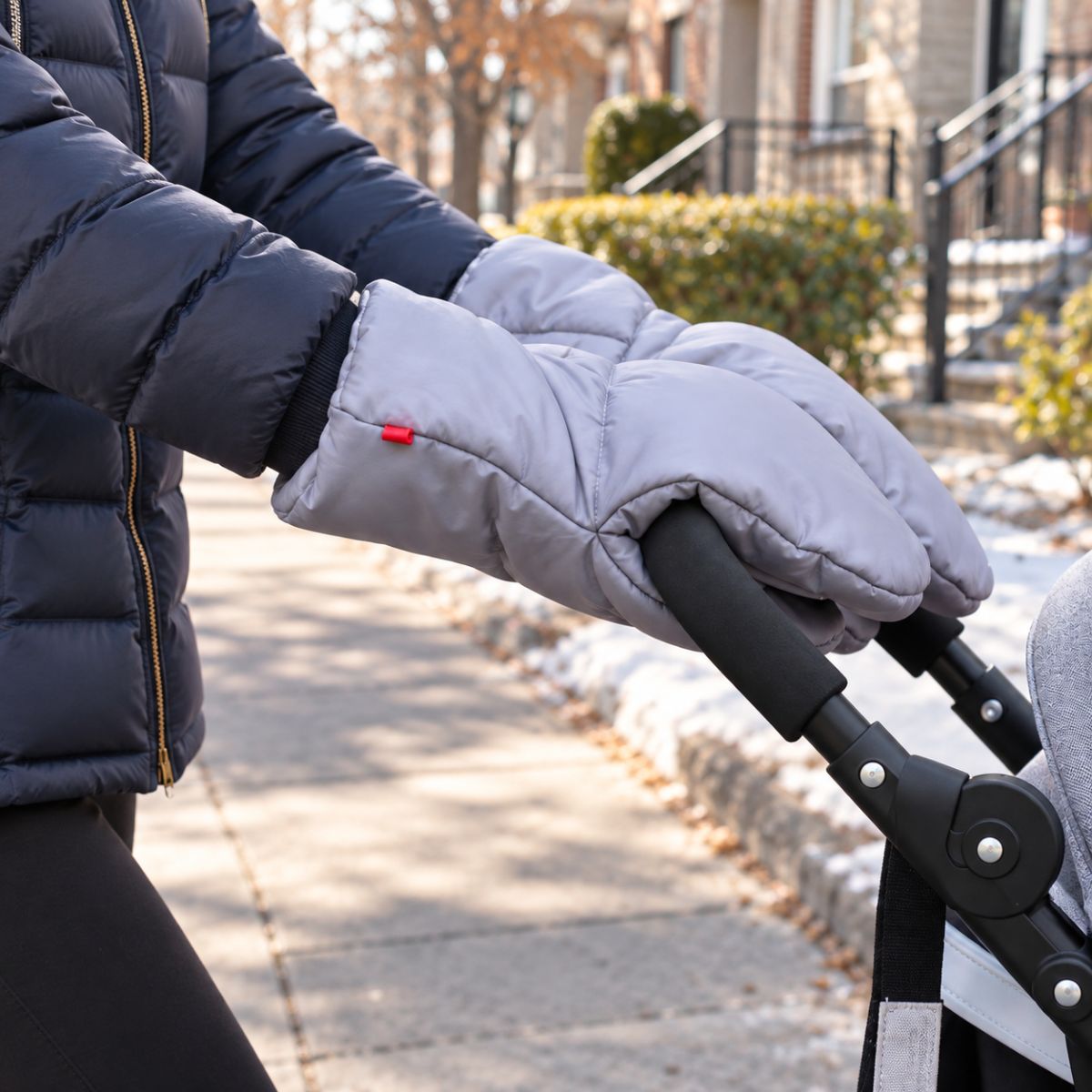 Gants pour poussette gris portés par un adulte en doudoune bleu marine pendant une promenade hivernale