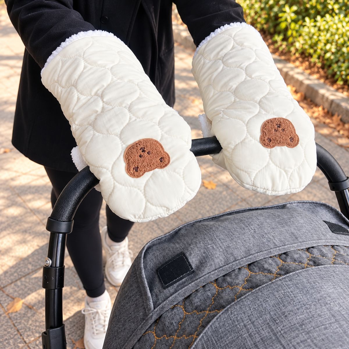 Vue de face des gants de poussette matelassés crème à motif ourson, fixés au guidon noir