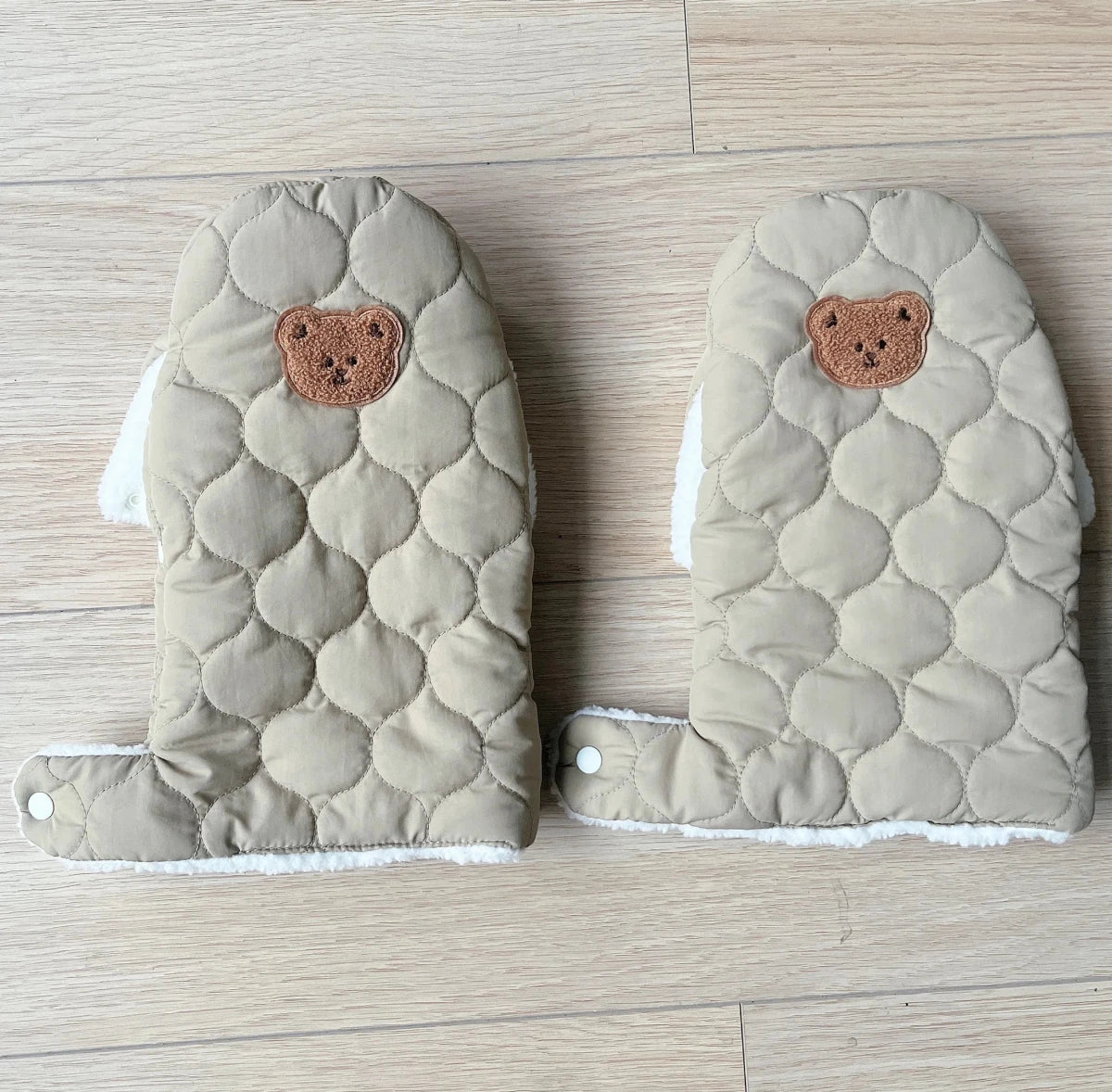 Paire de gants de poussette matelassés kaki clair avec écusson ourson marron et languettes à boutons-pression, vue de face