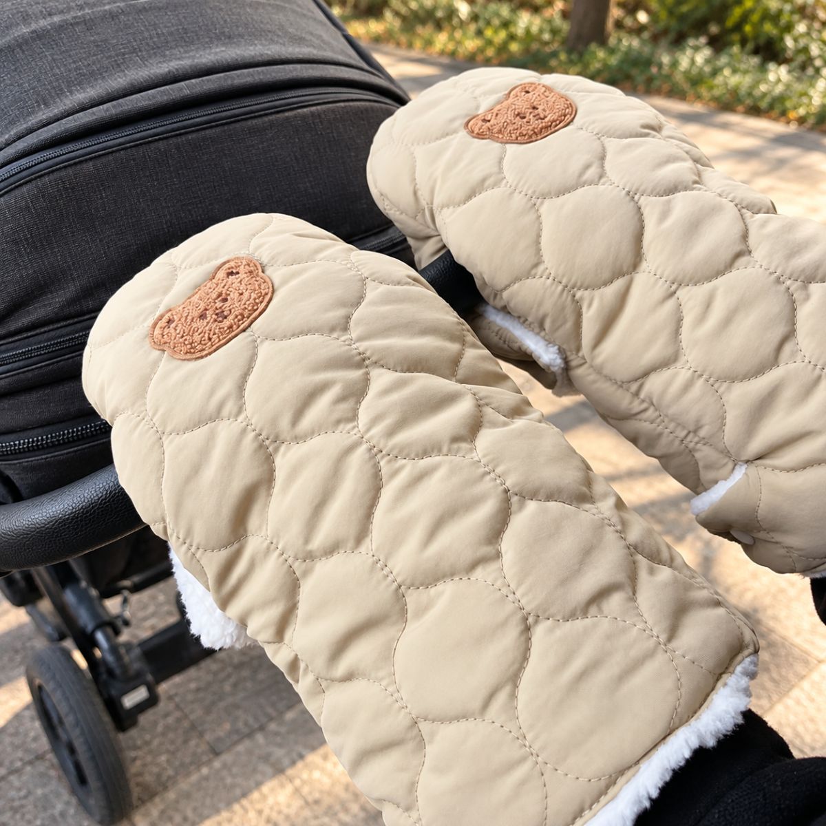 Gants de poussette matelassés kaki clair avec écusson ourson marron et doublure blanche, vue rapprochée au guidon