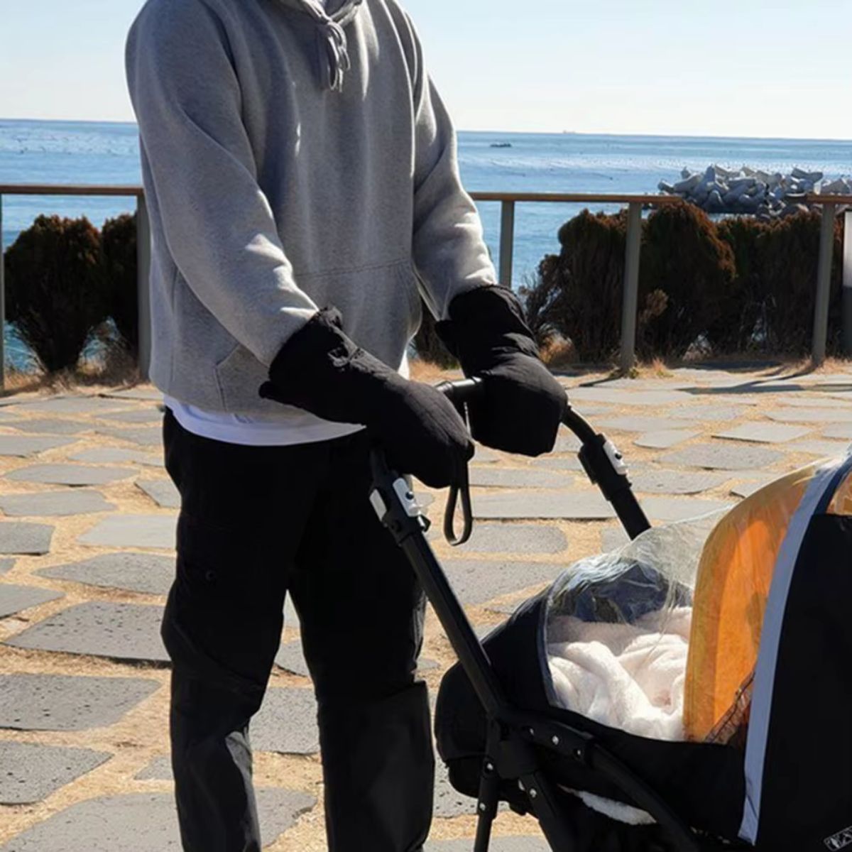 Gants de poussette noirs portés par un adulte poussant une poussette lors d'une promenade en bord de mer