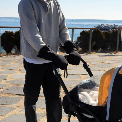 Gants de poussette noirs portés par un adulte poussant une poussette lors d'une promenade en bord de mer