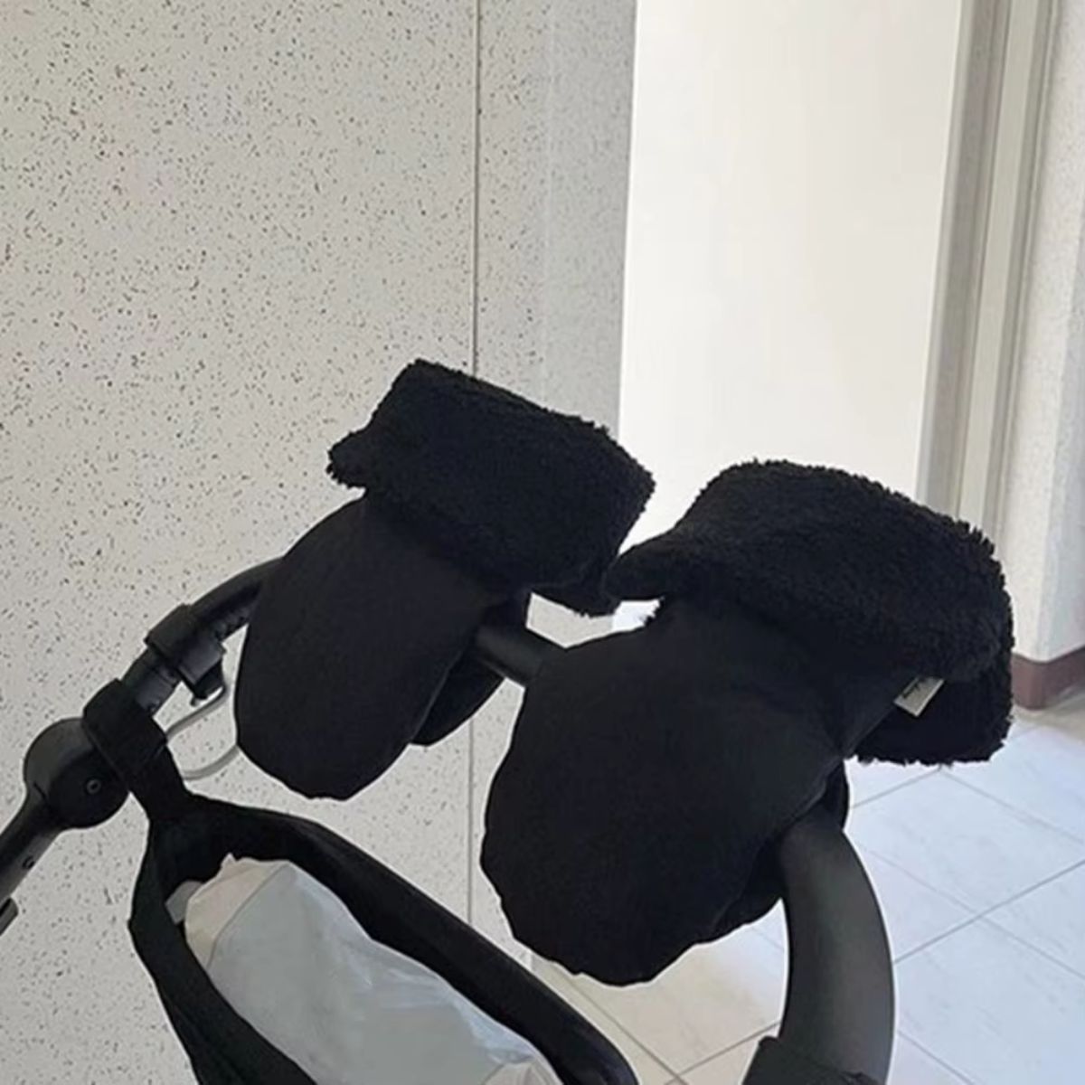 Vue latérale des gants de poussette texturés noirs avec revers pelucheux, placés sur un guidon courbé