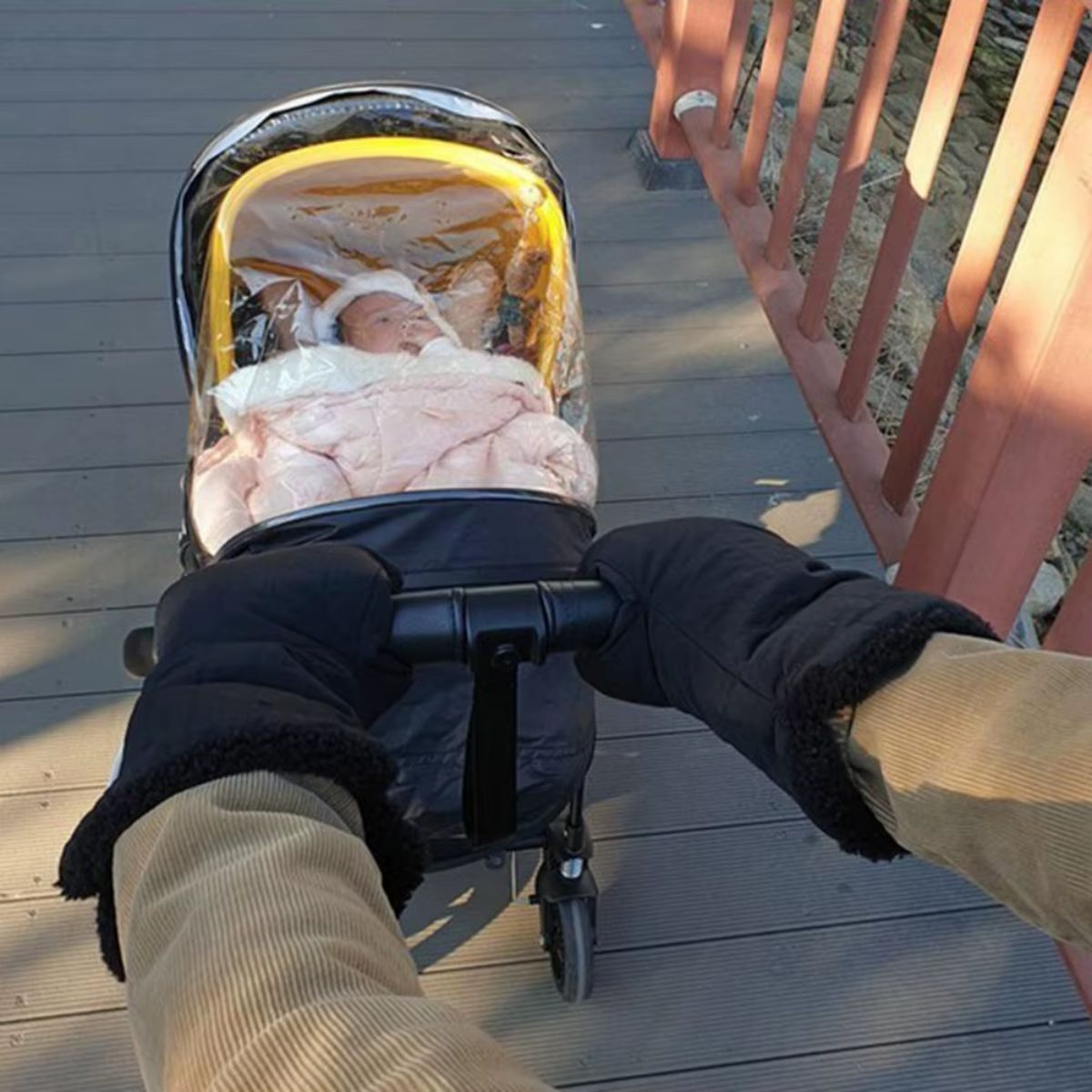 Vue des moufles de poussette noires à revers pelucheux, portées au guidon pendant une promenade avec bébé
