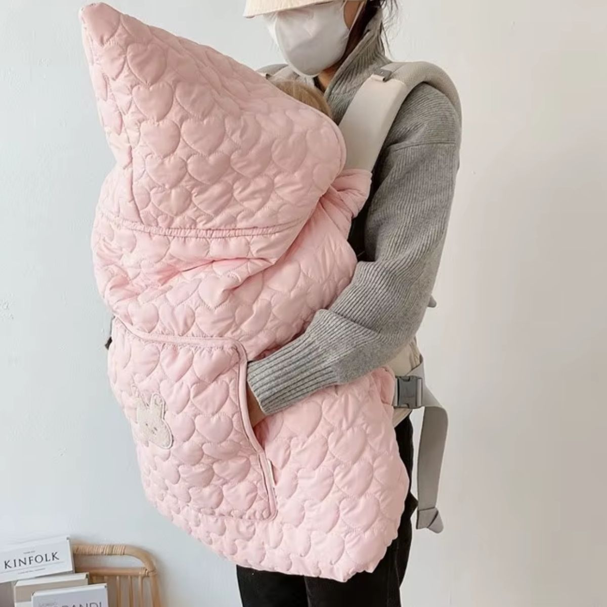 Cape porte-bébé rose poudré vue de profil, capuche pointue et tissu matelassé en cœurs