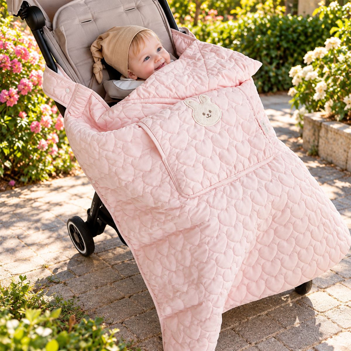 Couverture de poussette rose poudré avec motif lapin crème et matelassage en cœurs, bébé en promenade
