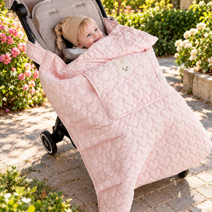 Couverture de poussette rose poudré avec motif lapin crème et matelassage en cœurs, bébé en promenade