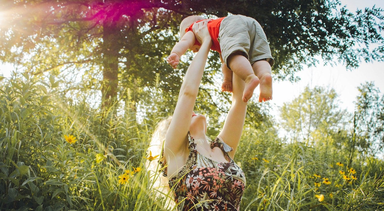 Une maman soulève tendrement son bébé en pleine nature, dans un moment complice baigné de lumière – image signature MamanPepite