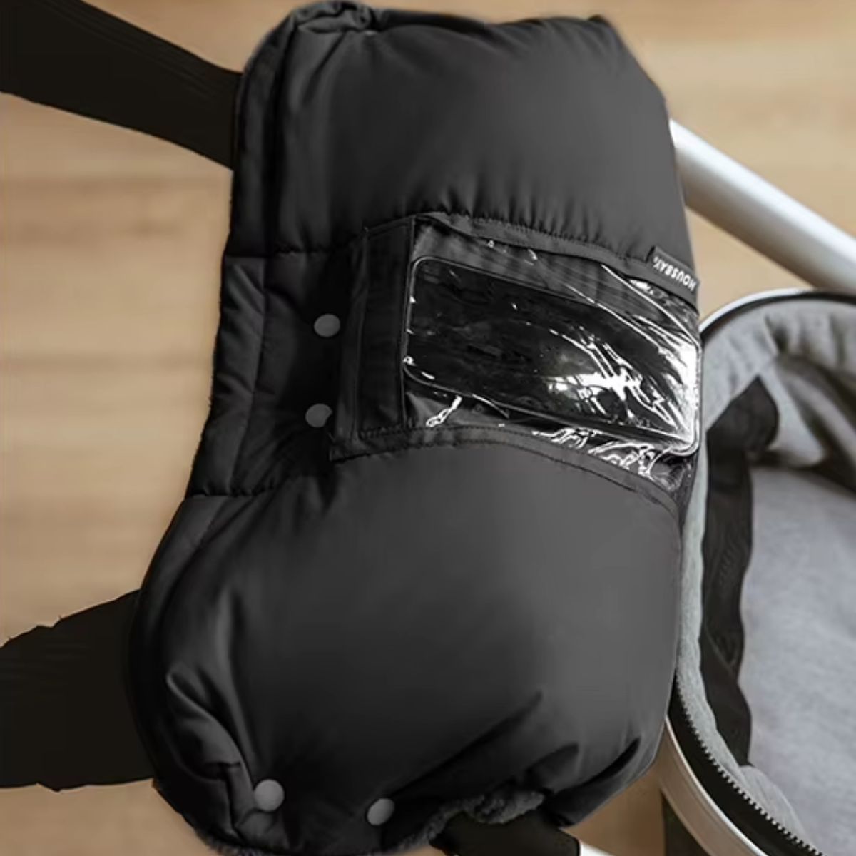 Gros plan du manchon poussette noir avec poche transparente pour smartphone et boutons-pression visibles