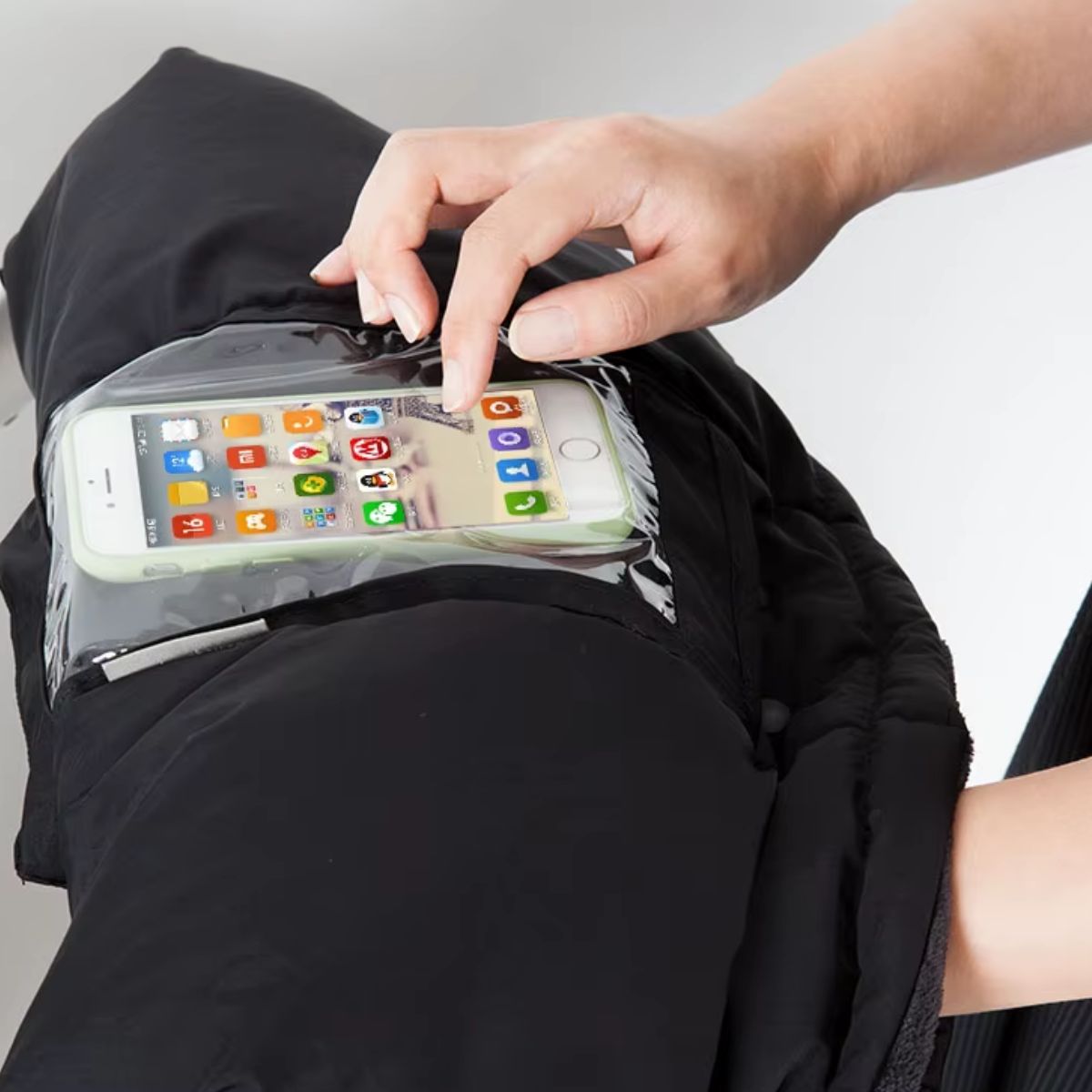Gros plan sur la poche téléphone transparente d'un manchon poussette noir, avec smartphone visible sous la fenêtre