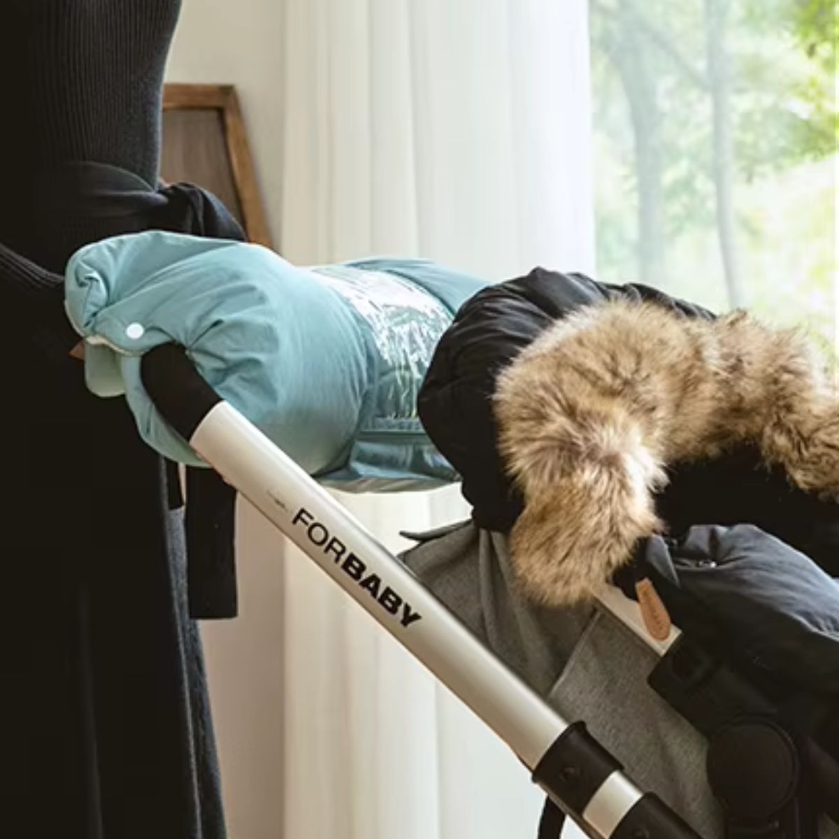 Manchon pour poussette turquoise avec poche téléphone transparente, porté au guidon d'une poussette