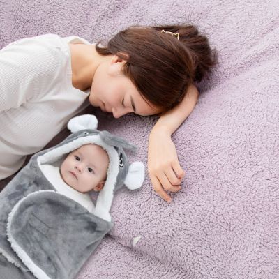 Maman allongée à côté de bébé enveloppé dans un nid d’ange gris, partageant un moment de tendresse et de douceur