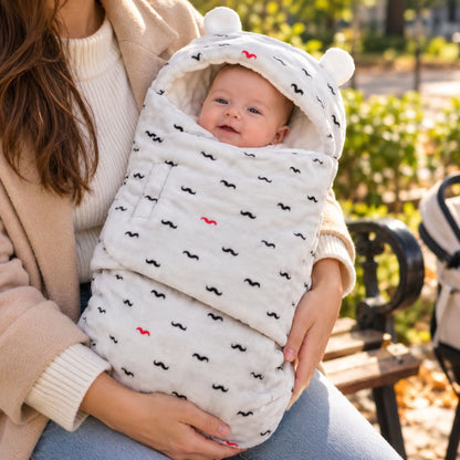 Nid d’ange bébé clair à petits motifs noirs, avec capuche arrondie à deux petites oreilles et rabat frontal, tenu dans les bras