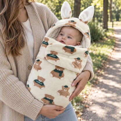 Nid d’ange bébé motif oursons écru avec capuche à longues oreilles de lapin et rabat frontal, tenu dans les bras