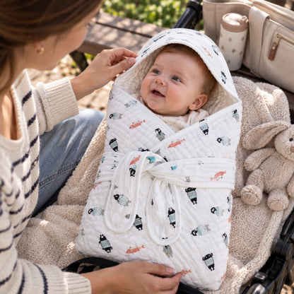 Bébé installé dans le nid d'ange gaze de coton à petits motifs, avec capuche intégrée et deux bandes de maintien, dans une poussette