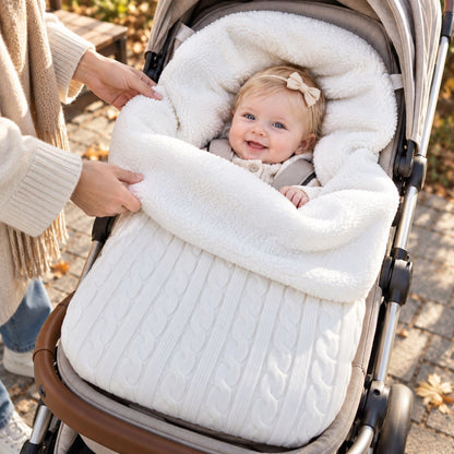 Nid d’ange polaire blanc cassé avec maille torsadée et large revers bouclé, bébé installé dans une poussette