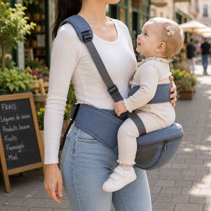 Porte-bébé à siège de hanche bleu avec sangle d’épaule et bande de maintien, porté de profil près d’un marché