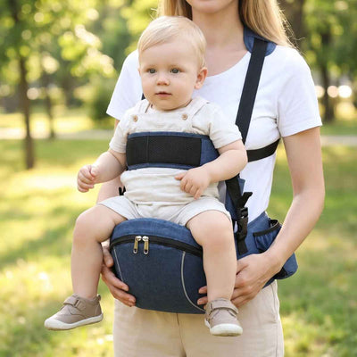 Porte-bébé à siège de hanche bleu marine avec sangle d’épaule et bande de maintien, porté de profil dans un parc