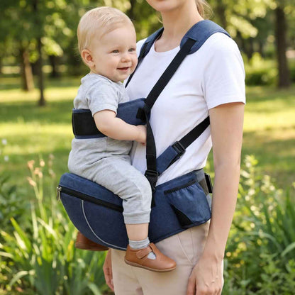 Porte-bébé à siège de hanche bleu marine avec sangle d’épaule et bande de maintien, porté face vers l’avant dans un parc