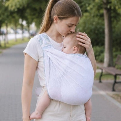 Porte-bébé à une épaule en maille blanche bleu gris avec assise large et sangle réglable, dans un parc
