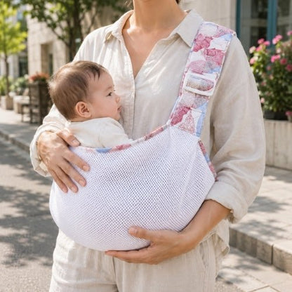 Porte-bébé à une épaule en maille blanche et rose avec assise large et sangle réglable, dans une rue
