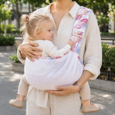 Porte-bébé à une épaule en maille blanche et rose avec assise large et sangle réglable, dans un parc