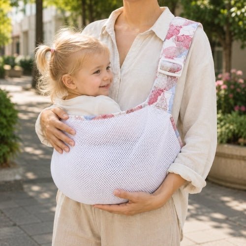 Porte-bébé à une épaule en maille blanche et rose avec assise large et sangle réglable, dans un jardin