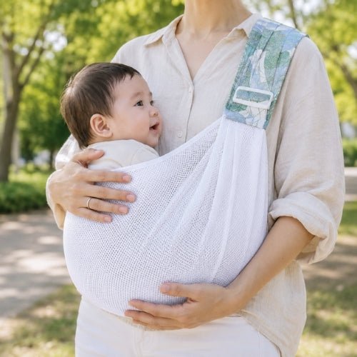 Porte-bébé à une épaule en maille blanche vert d’eau avec assise large et sangle réglable, dans un jardin