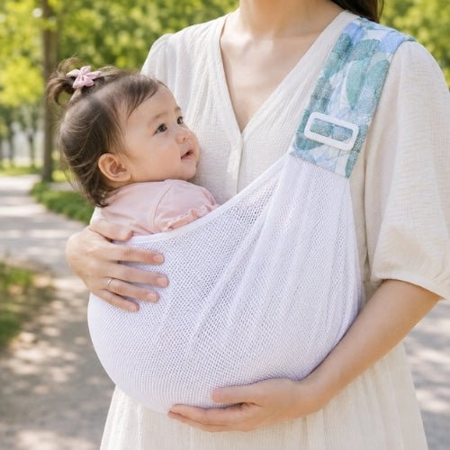 Porte-bébé à une épaule en maille blanche vert d’eau avec assise large et sangle réglable, dans un parc