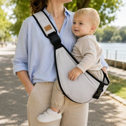Porte-bébé à une épaule gris clair avec sangle large et réglable, porté latéralement pendant une promenade