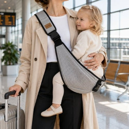 Porte-bébé à une épaule en maille gris clair avec sangle large et réglable, porté latéralement dans un aéroport
