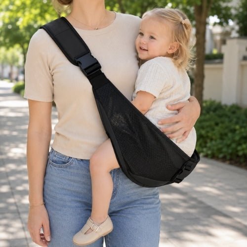Porte-bébé à une épaule en maille noire avec sangle large et réglable, porté latéralement dans un parc