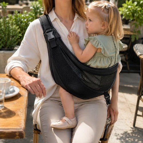 Porte-bébé à une épaule en maille noire avec sangle large et réglable, porté latéralement sur une terrasse
