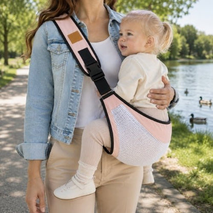 Porte-bébé à une épaule en maille rose avec sangle large et réglable, porté latéralement au bord d’un lac