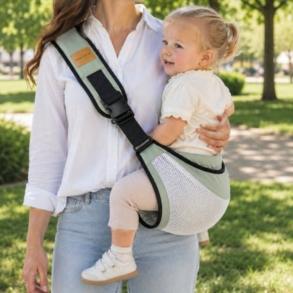 Porte-bébé à une épaule en maille vert sauge avec sangle large et réglable, porté latéralement dans un parc
