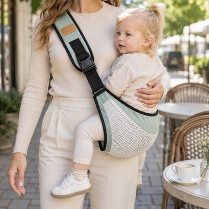Porte-bébé à une épaule en maille vert sauge avec sangle large et réglable, porté latéralement près d’une terrasse