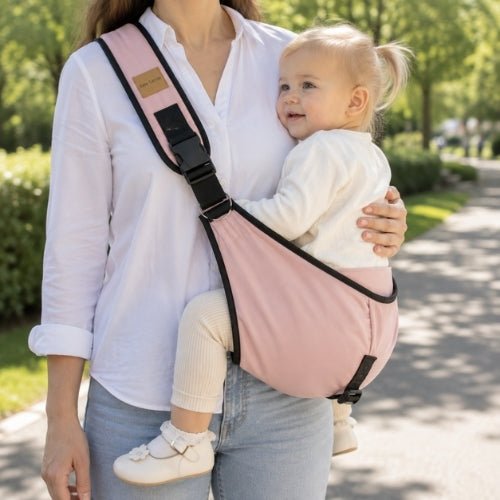 Porte-bébé à une épaule rose avec sangle large et réglable, porté latéralement dans un parc