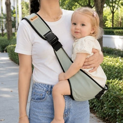 Porte-bébé à une épaule vert sauge avec sangle large et réglable, porté latéralement dans un parc